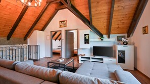 Ein Loft-Zimmer mit Holzbalkendecke, einer großen Couch, einem Fernseher und einem Essbereich.