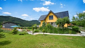 Ein gelbes Haus mit geneigtem Dach, umgeben von einem gepflegten Garten und einem Berg im Hintergrund.