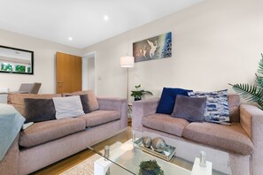 A living room with two sofas, a glass coffee table, a lamp, and a painting on the wall. - Heathrow Living 2BDR 2BA Apt 03-360stays (Stanwell)