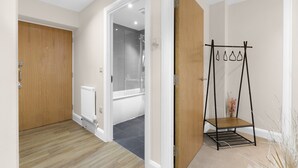 A hallway with a wooden door, a radiator, and a shower area. - Heathrow Living 2BDR 2BA Apt 03-360stays (Stanwell)