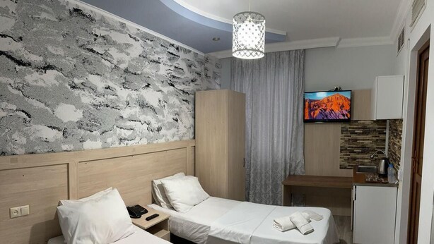 Habitación de hotel con dos camas, televisión, kitchenette pequeña y pared con diseño de piedra.