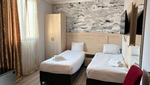 Quarto de hotel com duas camas, um guarda-roupa, uma televisão e parede com padrão marmorizado.