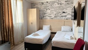 Quarto de hotel com duas camas, um guarda-roupa, uma televisão e parede com padrão de pedra.