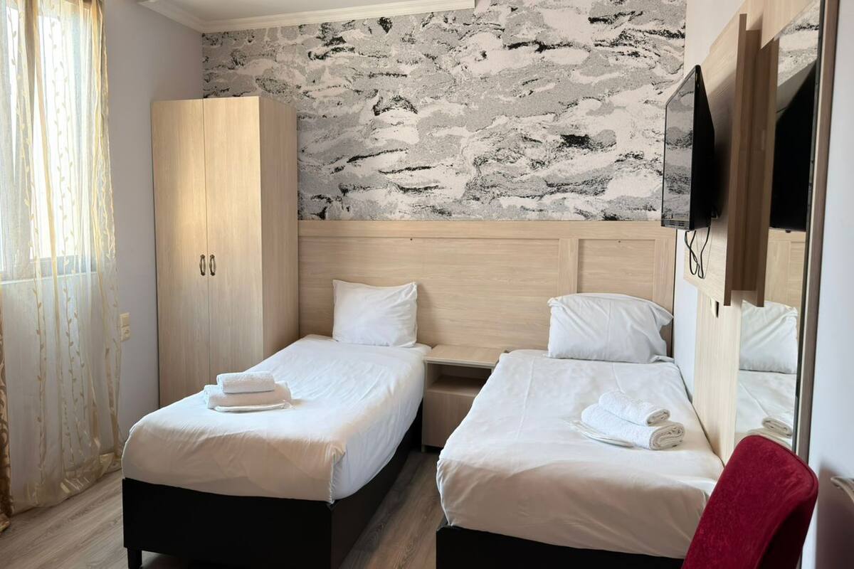 A hotel room with two beds, a wardrobe, a TV, and a stone-patterned wall.