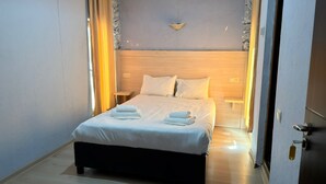 Una cama bien hecha con sábanas y toallas blancas, un cabecero de madera y una lámpara de pared.