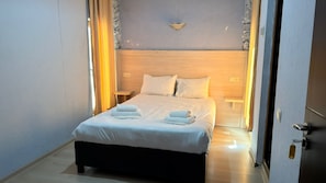 A neatly made bed with white linens and towels, a wooden headboard, and a wall-mounted light fixture. - Akman Swiss Hotel (Batumi)