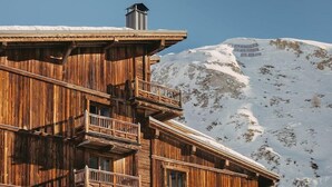 A wooden building with balconies, a chimney, and a snow-covered mountain in the background.