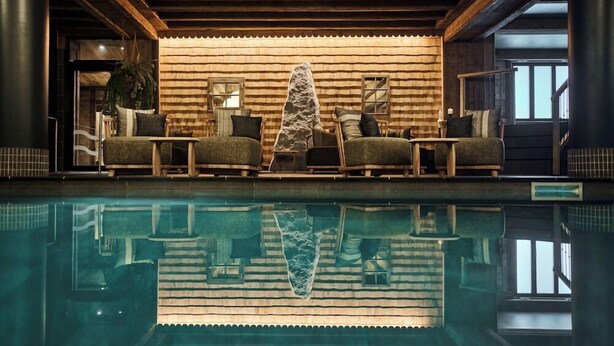 A pool area with a wooden ceiling, a stone sculpture, and a reflection of the room in the water.