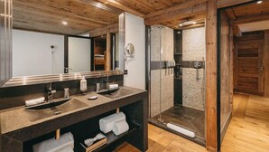 A modern bathroom with a wooden ceiling, a large mirror, a sink with a towel rack, and a walk-in shower.