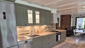 Une cuisine moderne dotée d’appareils électroménagers en acier inoxydable, de meubles de couleur verte et d’un mur en briques.