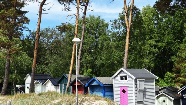Une rangée de cabanes de plage aux couleurs de toits différentes, avec un lampadaire au premier plan.
