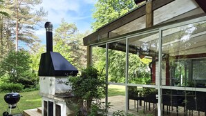 Une terrasse avec un barbecue, un coin repas fermé par des baies vitrées et une plateforme en bois.