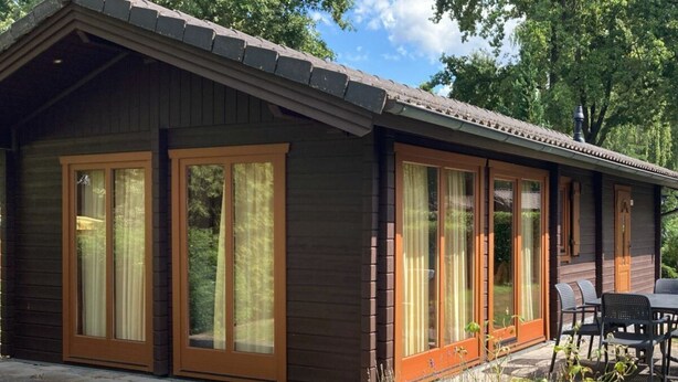 A wooden cabin with large sliding glass doors, a patio with outdoor furniture, and a garden area. - Holiday Home in Susteren With Terrace (Susteren)