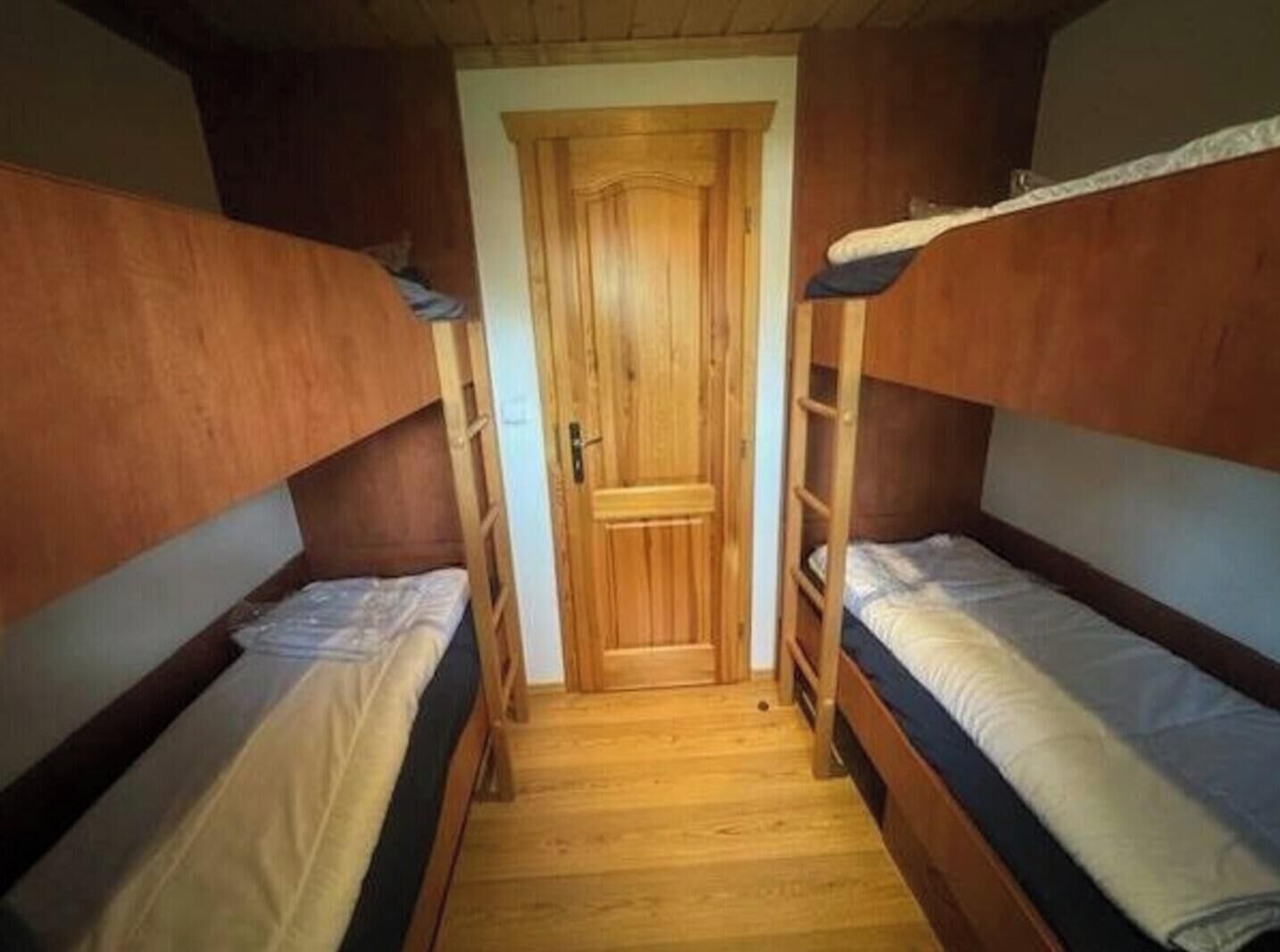 Ein schmales Zimmer mit zwei Etagenbetten, einer Holztür und Holzboden.