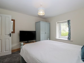 Ein Schlafzimmer mit Bett, Fernseher, Kleiderschrank und einem Fenster mit Vorhängen.