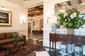 A lobby with a checkered floor, a sofa, a coffee table, a decorative vase, and a painting on the wall.