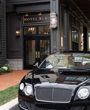 Un coche de lujo negro estacionado frente a un edificio con un cartel que dice 'HOTEL BURG'.
