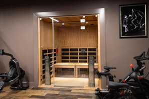 Un gimnàs amb equip d'exercici, una sauna de fusta i un quadre encimbellat a la paret.