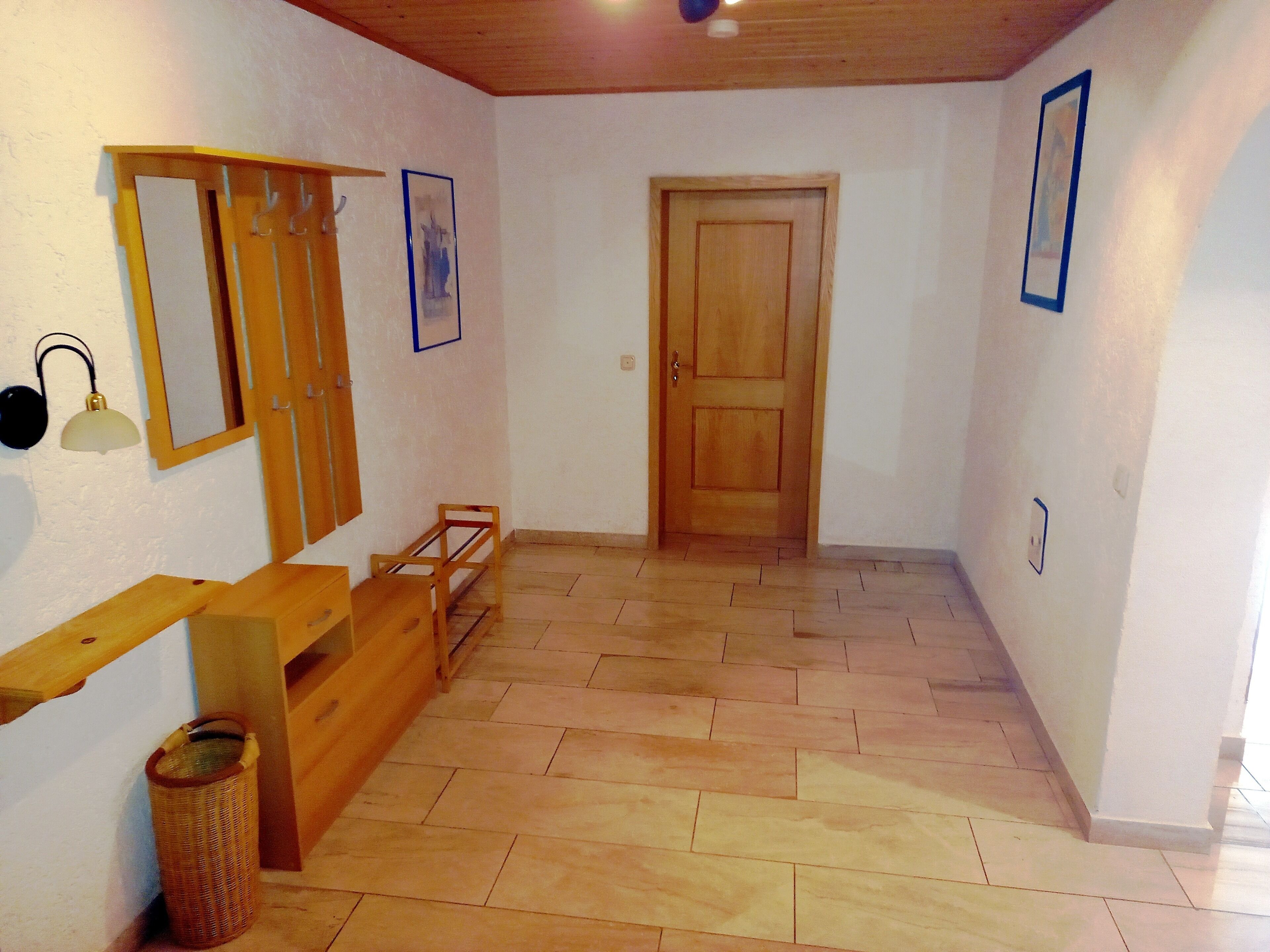 A hallway with wooden flooring, a wooden bench, a door, and a wall-mounted lamp.