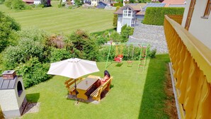 Een achtertuin met een patio, een parasol, een schommel en een klein speelgedeelte.