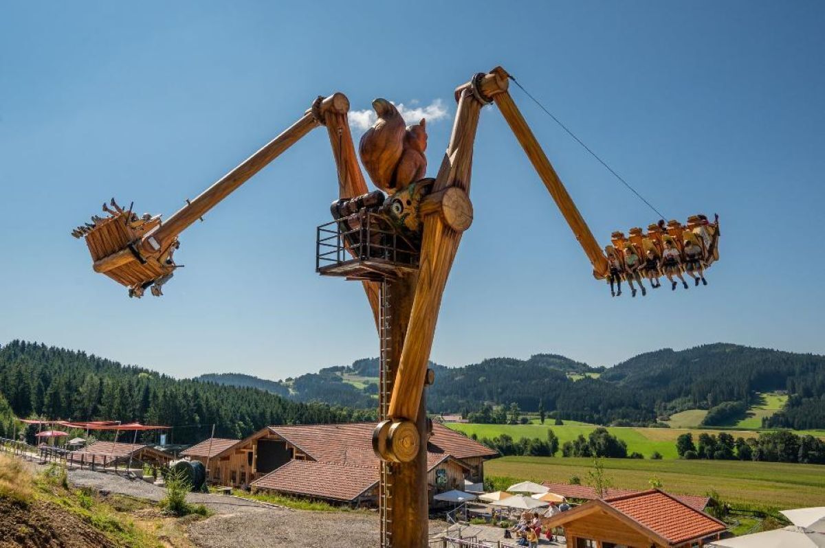 A wooden swing ride with a clear view of the surrounding rural landscape and buildings.
