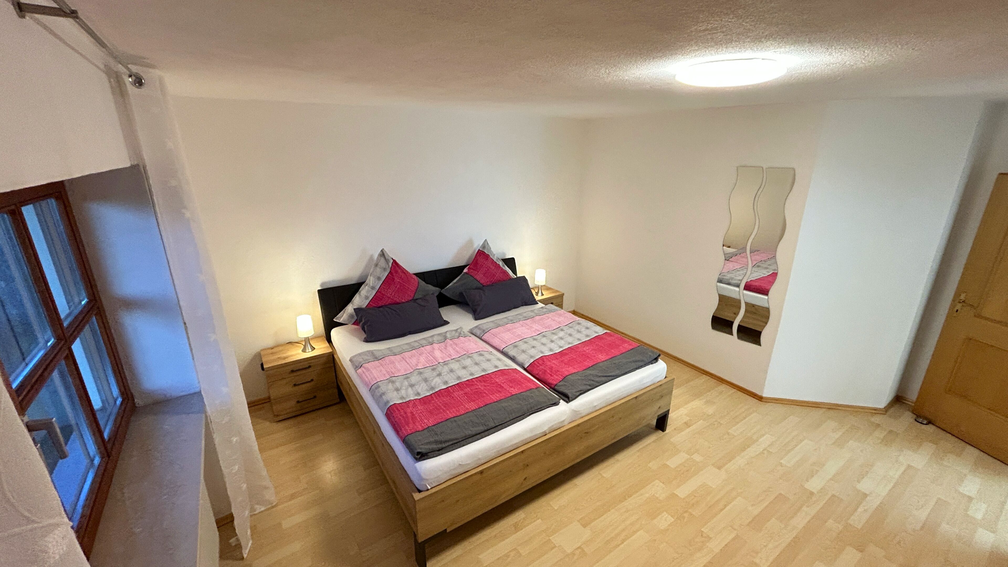 A bedroom with a wooden bed, bedside tables, a mirror, and a window.