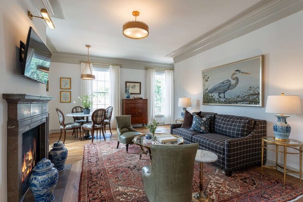 A living room with a fireplace, sofa, chairs, a table, and a painting of a bird. - Wine Country Stay | Sauna, Rooftop Views + Dining (Leesburg)