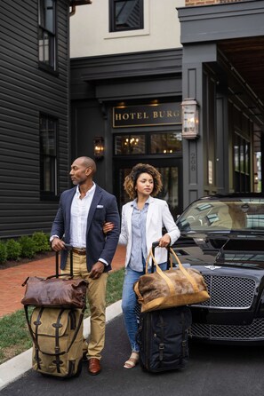 A man and a woman walking towards a building labeled 'HOTEL BURG' with luggage. - Close to Wineries + Pet Friendly & On Site Dining (Leesburg)