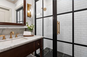 A bathroom with a marble sink, gold fixtures, a mirror, and a shower with black and white tiles. - Close to Wineries + Sauna & On Site Dining (Leesburg)