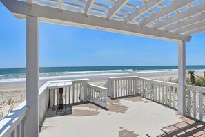 Une vue sur la plage depuis une véranda couverte, dotée d’une balustrade, d’un sol en béton et surplombant un ciel bleu dégagé.