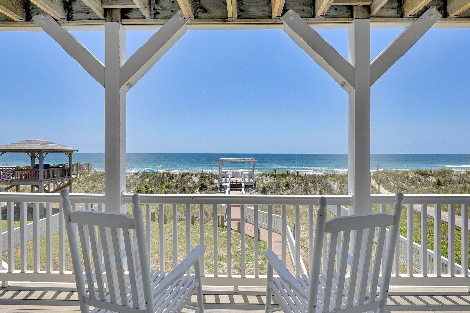 A covered outdoor area with white chairs and a view of the beach.