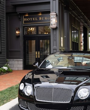 A black luxury car parked in front of a building with a sign reading 'HOTEL BURG.'