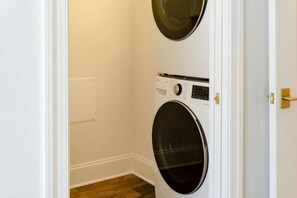 Una sala de bugaderia amb dues piles de rentadores i assecadores, una porta blanca i un terra de fusta.