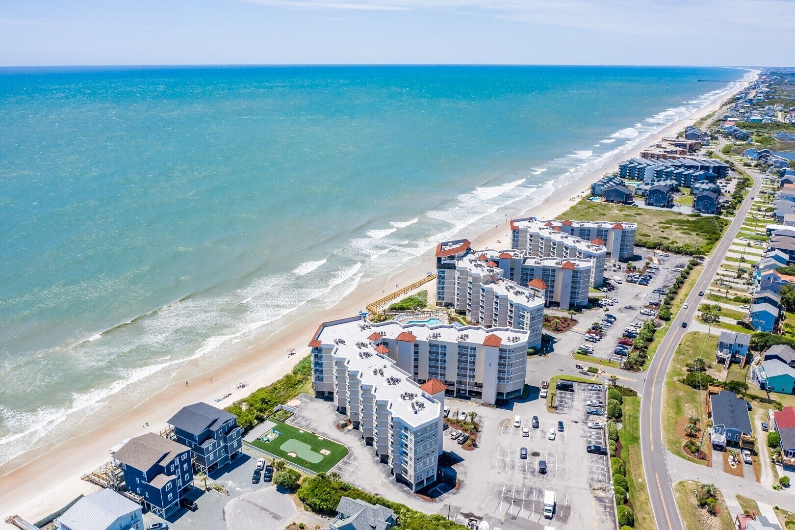 Ein Küstenhotel mit mehreren Gebäuden, direkt am Strand und einem Parkplatz.