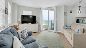 A living room with a TV, sofa, and a balcony with a view. - 1 Bedroom Overlooking Atlantic Ocean and Swimming Pool (North Topsail Beach)