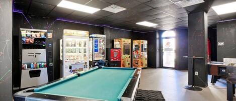 A pool table in a room with arcade games and vending machines.