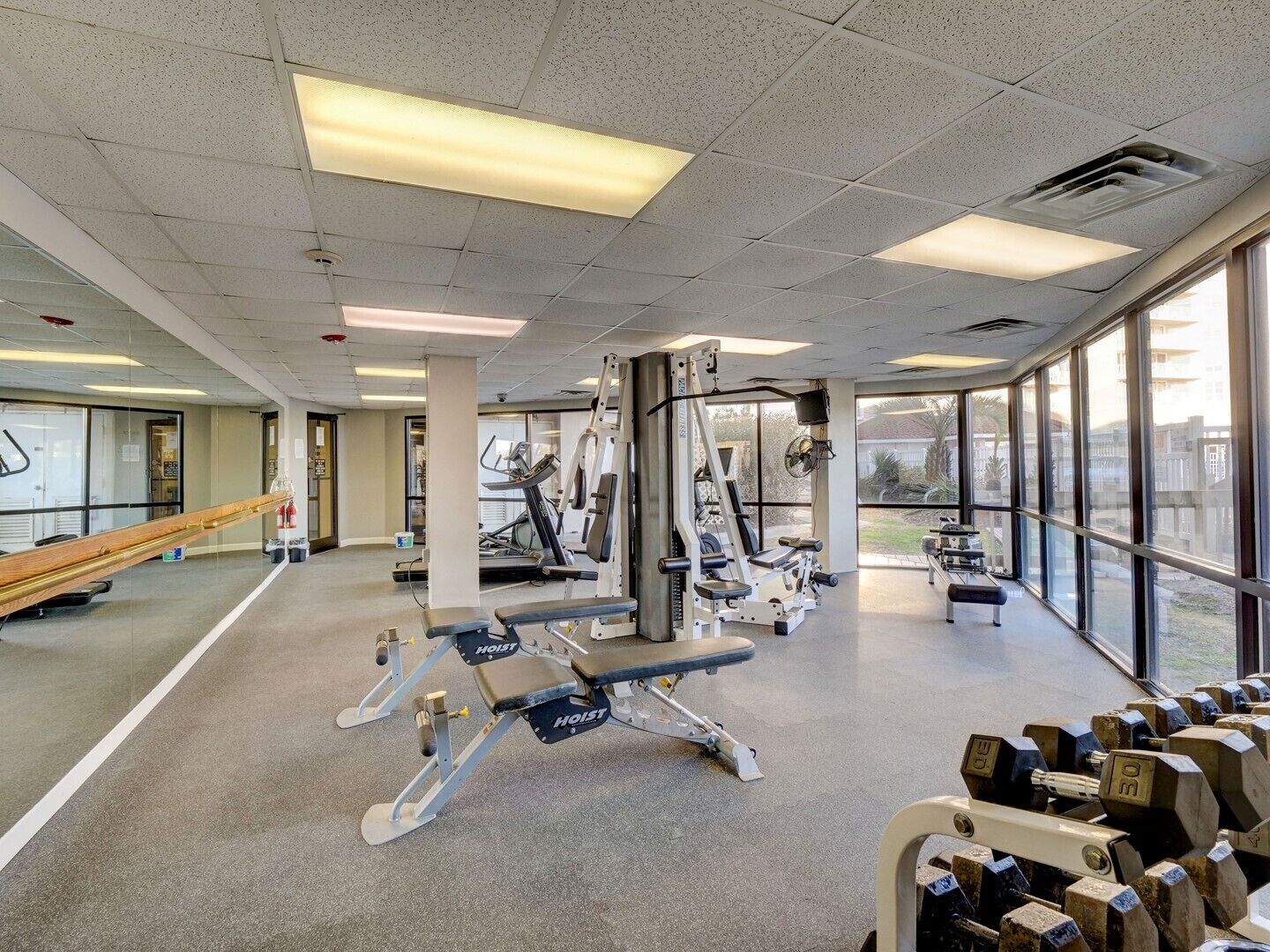 A gym with exercise equipment, large windows, and a mirror.