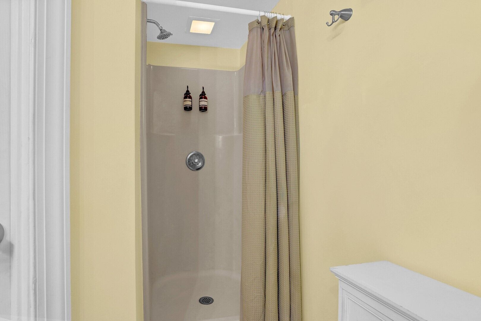 A shower with a beige curtain, a white wall, and a small bottle on the wall.