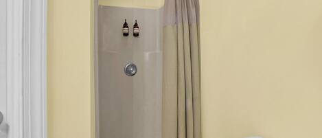 A shower with a beige curtain, a white wall, and a small bottle on the wall.