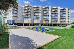 Ein mehrstöckiges Wohngebäude mit Balkonen, einem Parkplatz und einem Erholungsbereich mit Rasen und Gartenmöbeln.