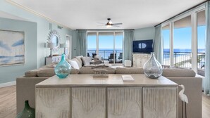Un soggiorno con un'ampia finestra, un ventilatore a soffitto e vista sull'oceano.