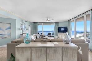 A living room with a large window, a ceiling fan, and a view of the ocean.