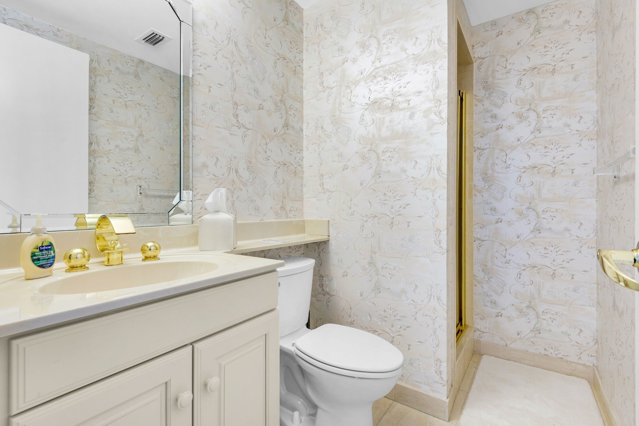 A bathroom with a white sink, gold faucets, a toilet, and a shower with a gold frame.
