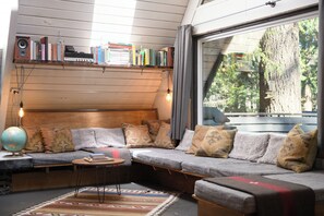 Ein gemütlicher Raum mit Holzbalkendecke, einer eingebauten Couch mit Kissen, einem kleinen Tisch, einem Globus und einem Bücherregal mit Büchern und einer Lampe.