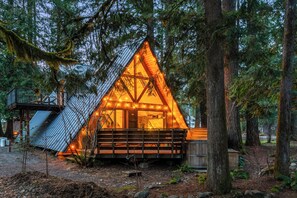 Eine dreieckige Holzhütte mit Veranda, umgeben von Bäumen.