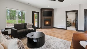 A modern living room with a fireplace, a large window, and a ceiling fan.