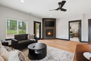 A modern living room with a fireplace, a large window, and a ceiling fan.
