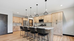 A modern kitchen with wooden cabinets, a central island with bar stools, stainless steel appliances, and pendant lighting.