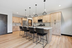 A modern kitchen with wooden cabinets, a central island with bar stools, stainless steel appliances, and pendant lighting.