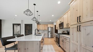 A modern kitchen with wooden cabinets, a central island, stainless steel appliances, and pendant lighting.